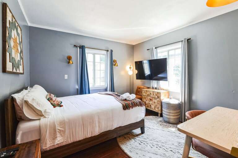 Relax in our queen bedroom featuring a large wall-mounted TV, perfect for unwinding with your favorite shows and movies. A dedicated workspace is also provided in each bedroom. Relax in our queen bedroom featuring a large wall-mounted TV, perfect for unwinding with your favorite shows and movies. A dedicated workspace is also provided in each bedroom.